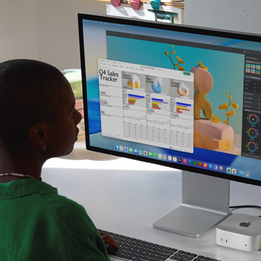 Woman working on an Excel spreadsheet on a Mac, sitting at a work table. The Excel spreadsheet is a Q4 sales tracker. Behind the Excel spreadsheet window is a Pixelmator Pro window.