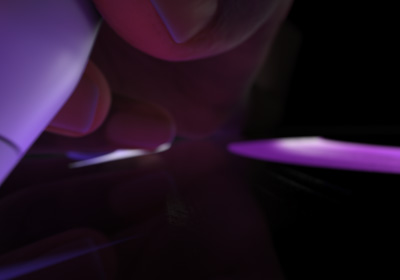 Mão a segurar o Apple Pencil Pro em posição de escrita. A ponta toca no ecrã onde são desenhadas pinceladas espessas em roxo vivo.