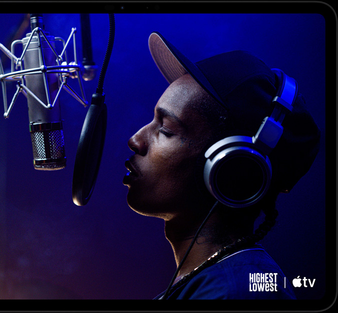 iPad Pro, landscape orientation, front exterior, space black colour, rounded corners, black display bezel, display showing AppleTV+ playing a scene from  the Apple TV+ original film Highest 2 Lowest with ASAP Rocky as Yung Felon rapping into a microphone