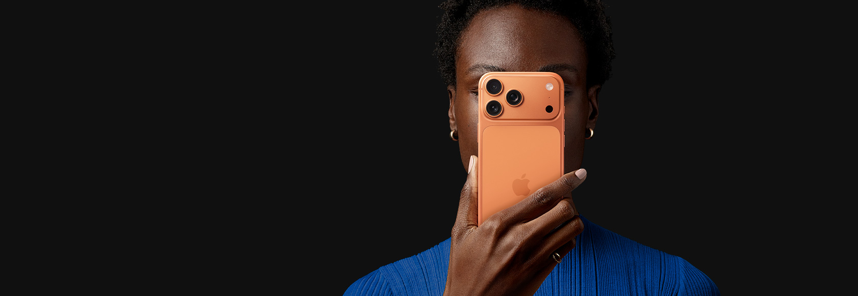 한 사람이 코스믹 오렌지 색상 iPhone 17 Pro를 뒷면이 바깥을 향하도록 얼굴 앞에 들고 있는 모습