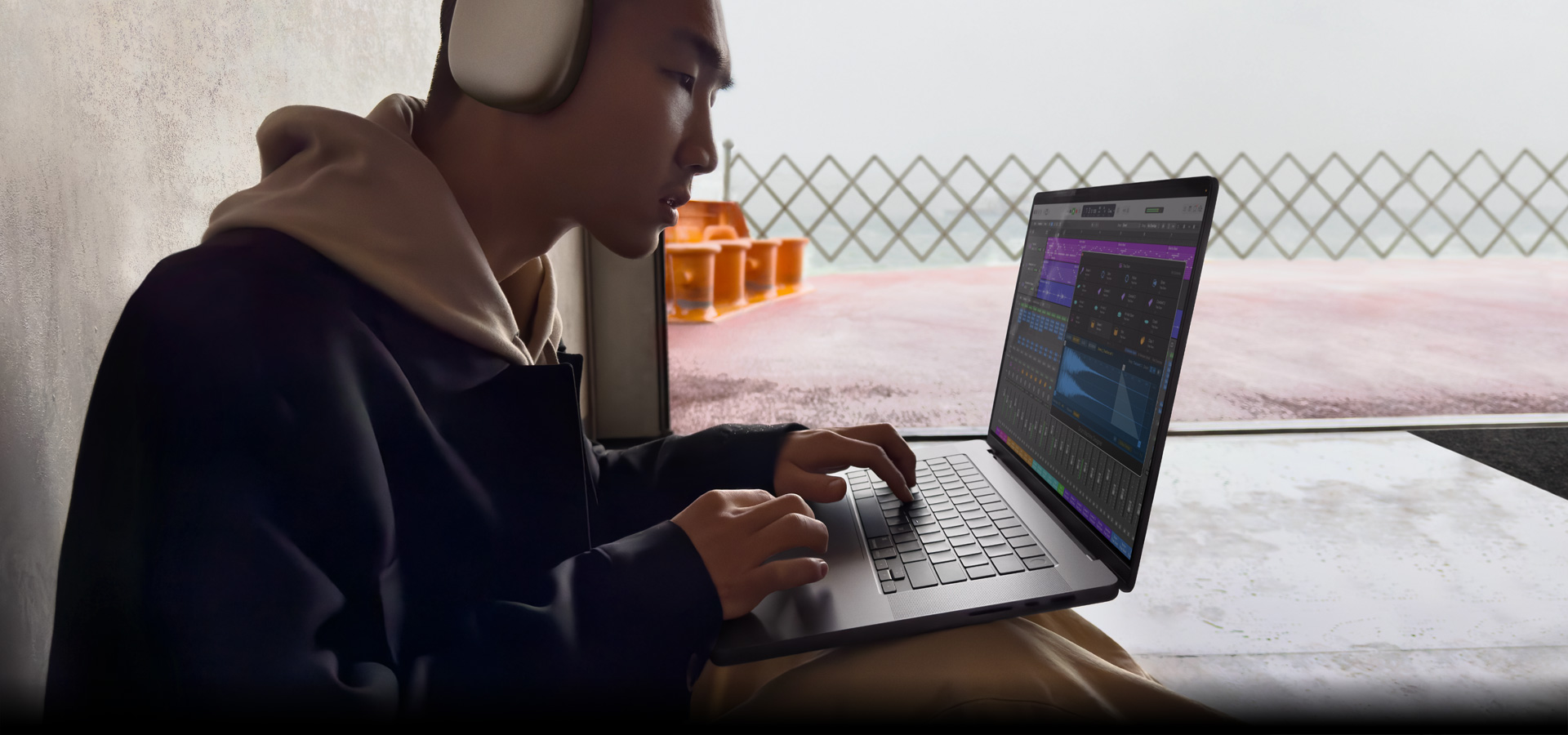 Side profile of a person wearing AirPods Max using Logic Pro on a MacBook Pro 16″, screen shows Logic Pro workspace