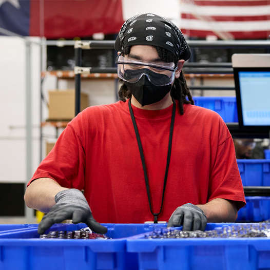 An employee wearing safety gloves, glasses and mask handles materials at a facility