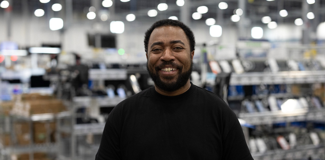 An employee stands in a logistics and repair centre, smiling at the camera