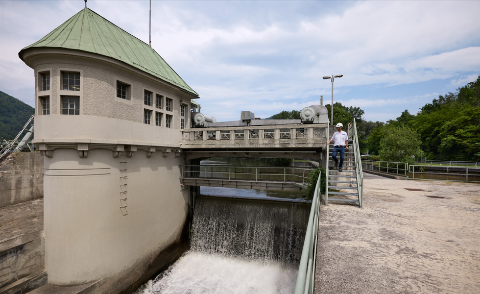 An employee wearing a safety hat descends stairs from a bridge at a hydroelectric facility