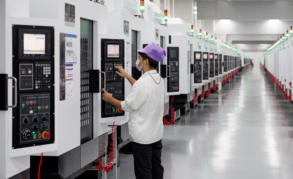 A uniformed employee presses buttons on a machine in a component manufacturing facility