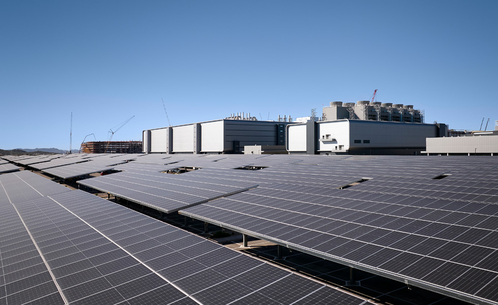 Rijen zonnepanelen naast een industrieel gebouw onder een heldere blauwe hemel