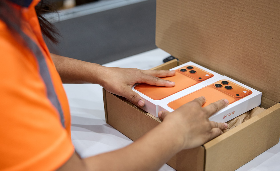Medewerker die iPhones in hun verpakking in een verzenddoos legt.
