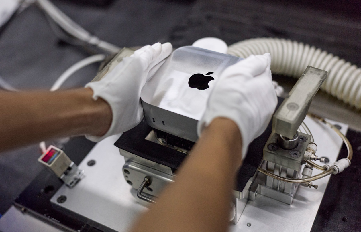 Handen met handschoenen aan leggen een Mac mini in een productiemachine tijdens de assemblage