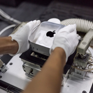 Handen met handschoenen aan leggen een Mac mini in een productiemachine tijdens de assemblage
