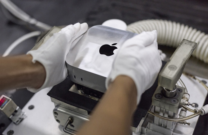 Handen met handschoenen aan leggen een Mac mini in een productiemachine tijdens de assemblage