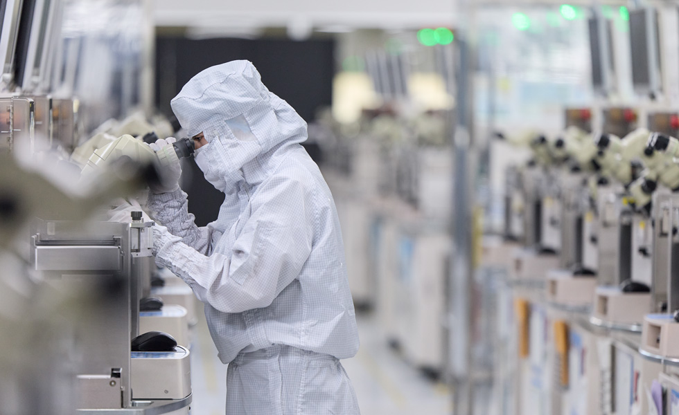 Een medewerker in uniform met mondkapje drukt op knoppen op productieapparatuur