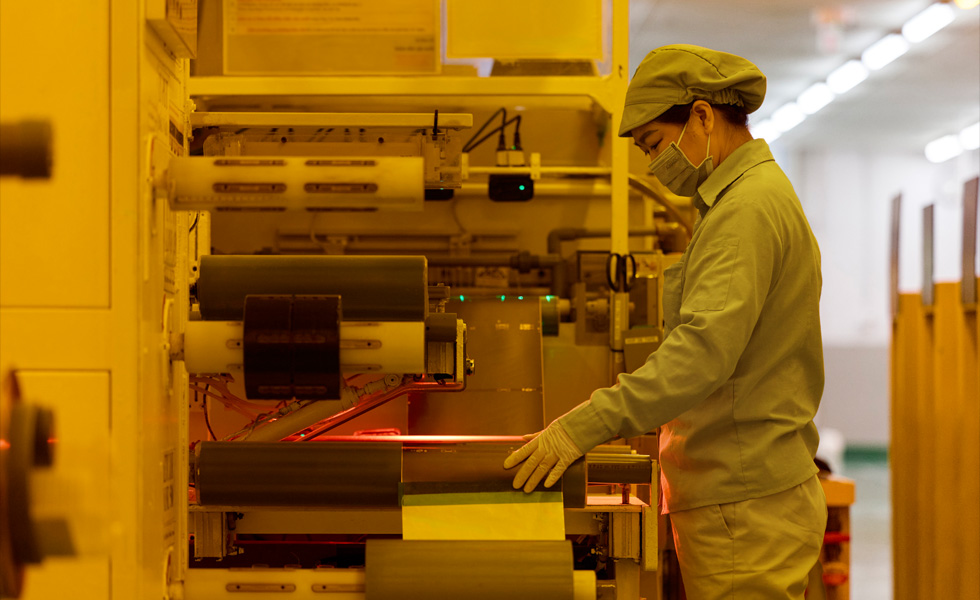 Een medewerker in uniform met mondkapje drukt op knoppen op productieapparatuur