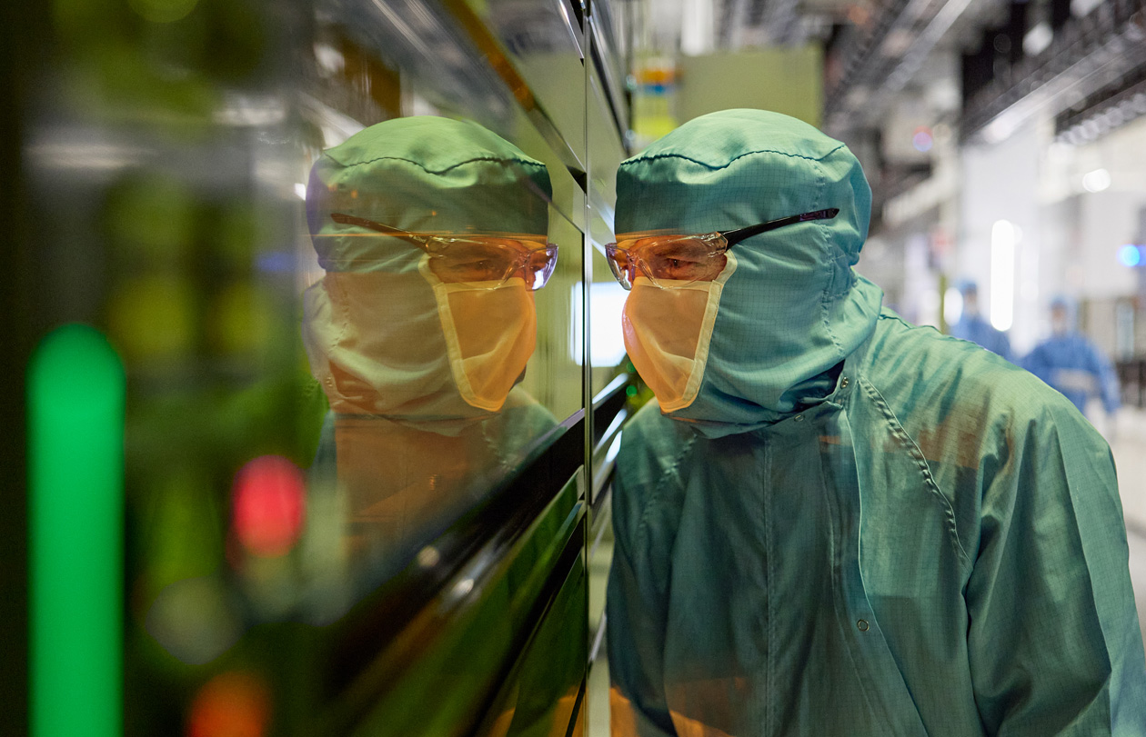 Een medewerker in volledig beschermende werkkleding kijkt door een raam van een productiemachine