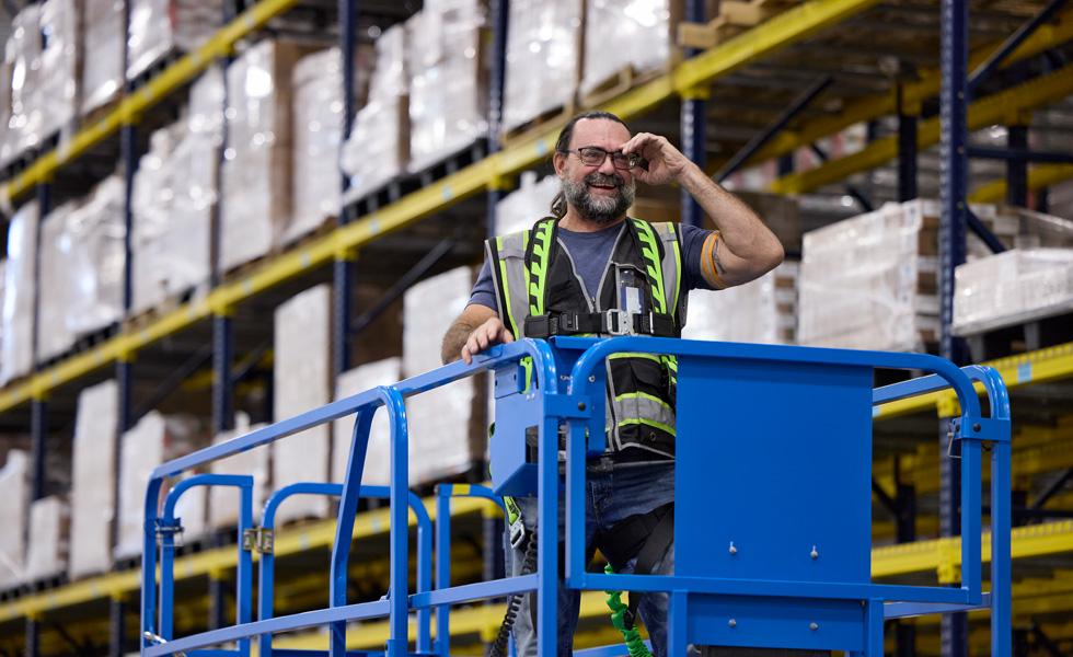 Een magazijnmedewerker met een veiligheidsvest rijdt in een bestuurbare lift