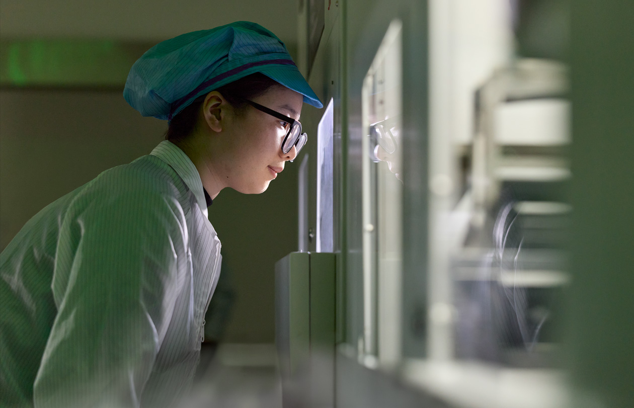 Een medewerker in volledig beschermende werkkleding en met een veiligheidsbril observeert de assemblage van Apple Watch