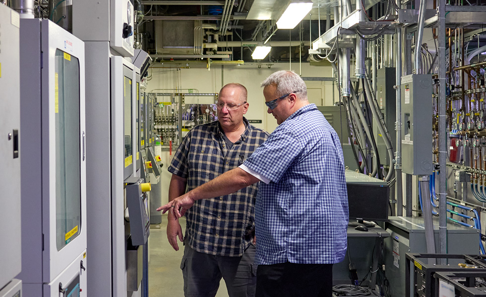 Twee mensen met veiligheidsbril praten bij machines