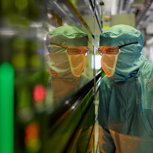 Een medewerker in volledig beschermende werkkleding kijkt door een raam van een halfgeleidermachine