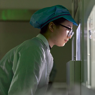 Een medewerker in volledig beschermende werkkleding en met een veiligheidsbril observeert de assemblage van Apple Watch