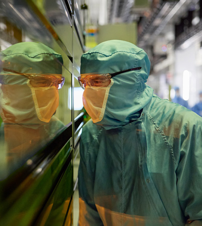 Een medewerker in volledig beschermende werkkleding kijkt door een raam van een halfgeleidermachine