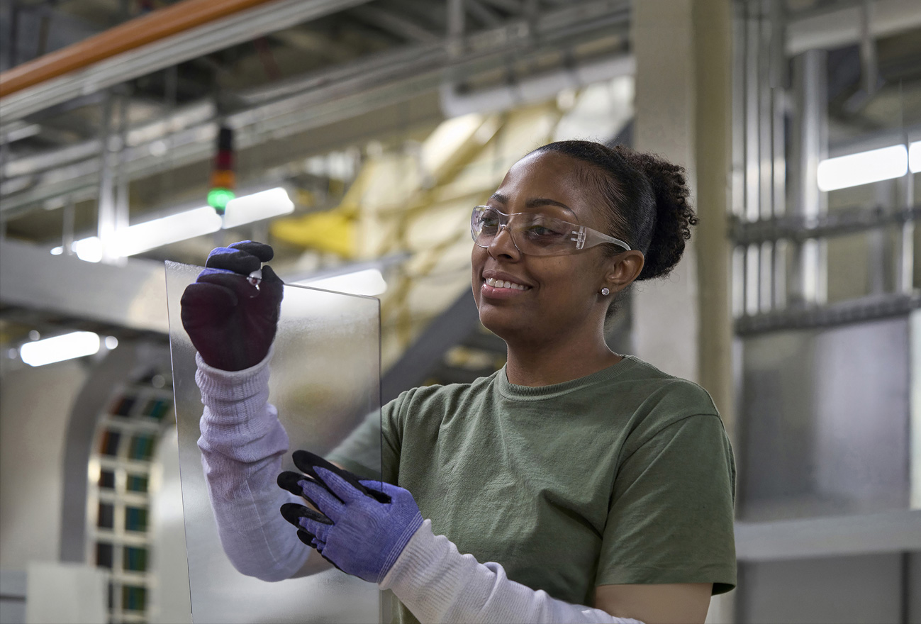 Een medewerker met een veiligheidsbril inspecteert een glazen component in een assemblagefabriek